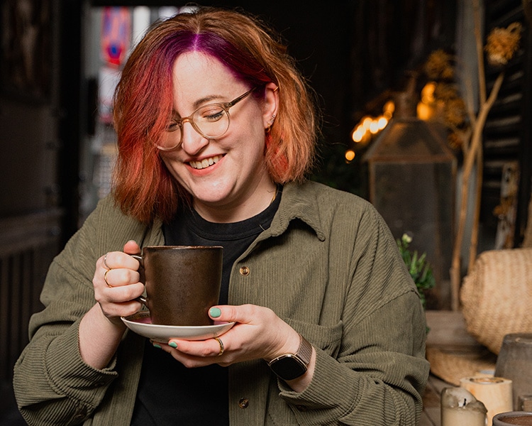 Birte Kahrs holding a cup and saucer with both her hands, looking down at the cup smiling