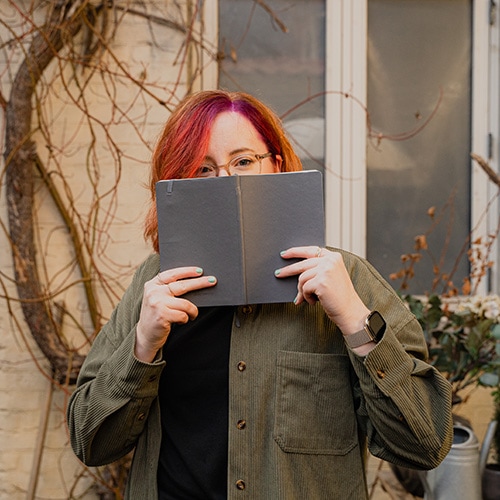 Birte Kahrs hiding half her face with a notebook that she holds open with both her hands